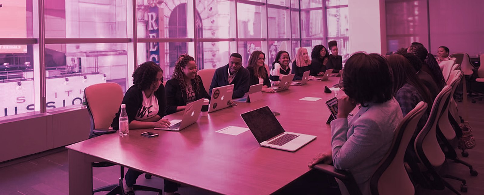 A team around a boardroom table with laptops, in pink light